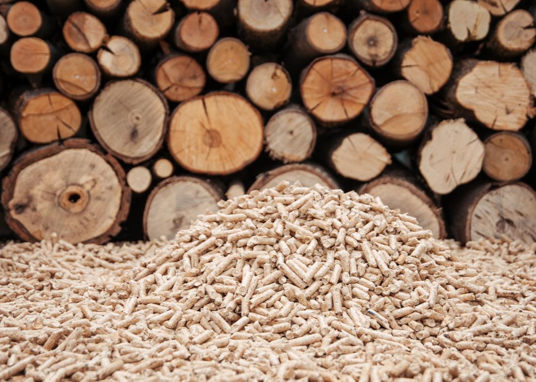 A large pile of wood pellets in front of a backdrop of stacked logs