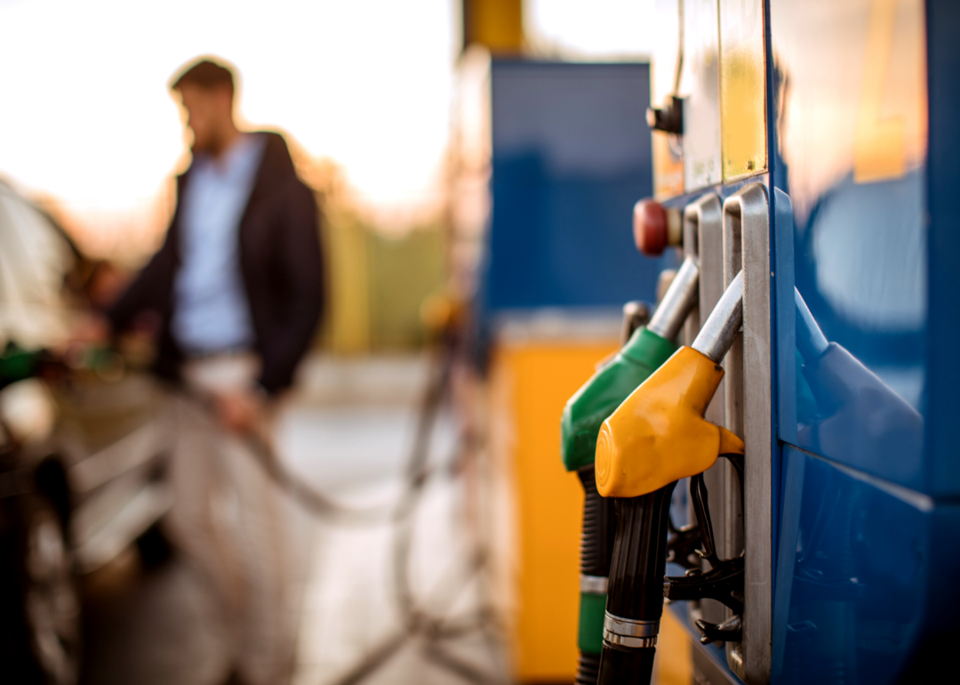 A man pumping gas with green and yellow gas pumps in the foreground