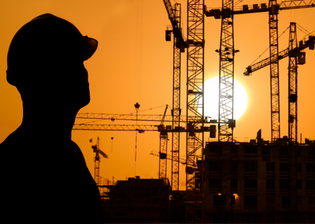 Silhouette of a construction worker against a sunset with a backdrop of cranes