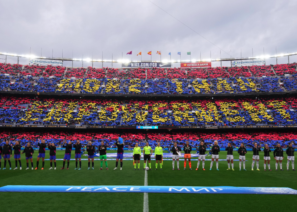 Players of FC Barcelona and Real Madrid line up as fans perform a tifo in the stands 