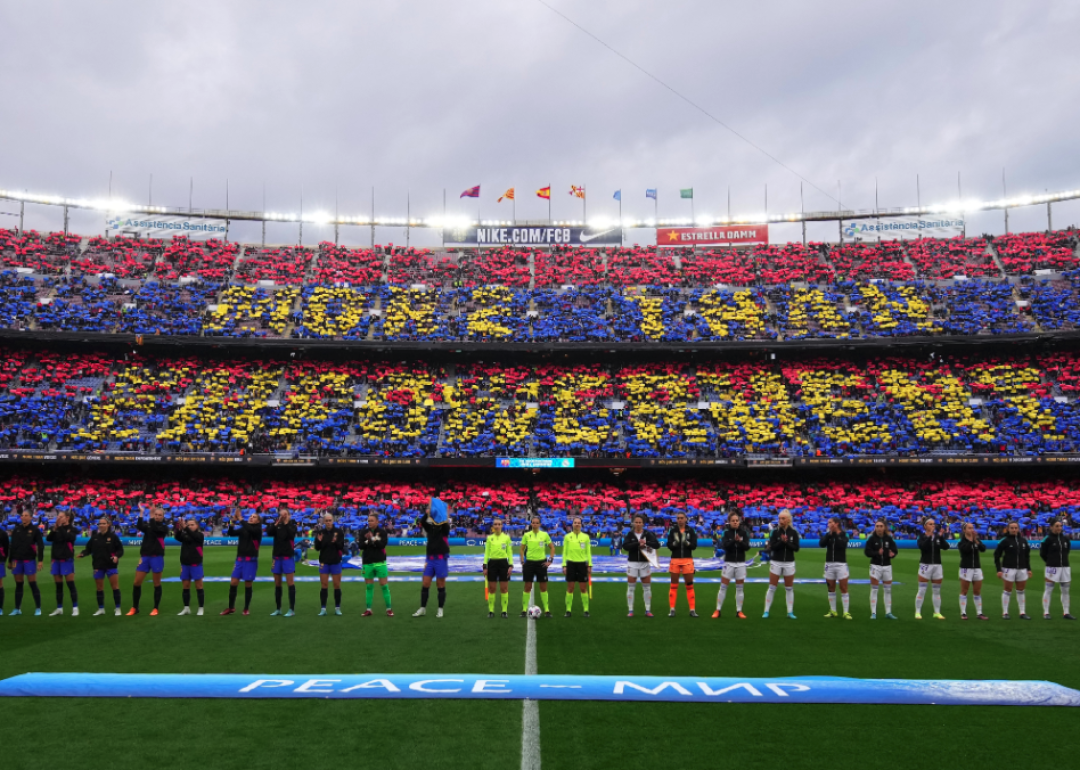 Players of FC Barcelona and Real Madrid line up as fans perform a tifo in the stands