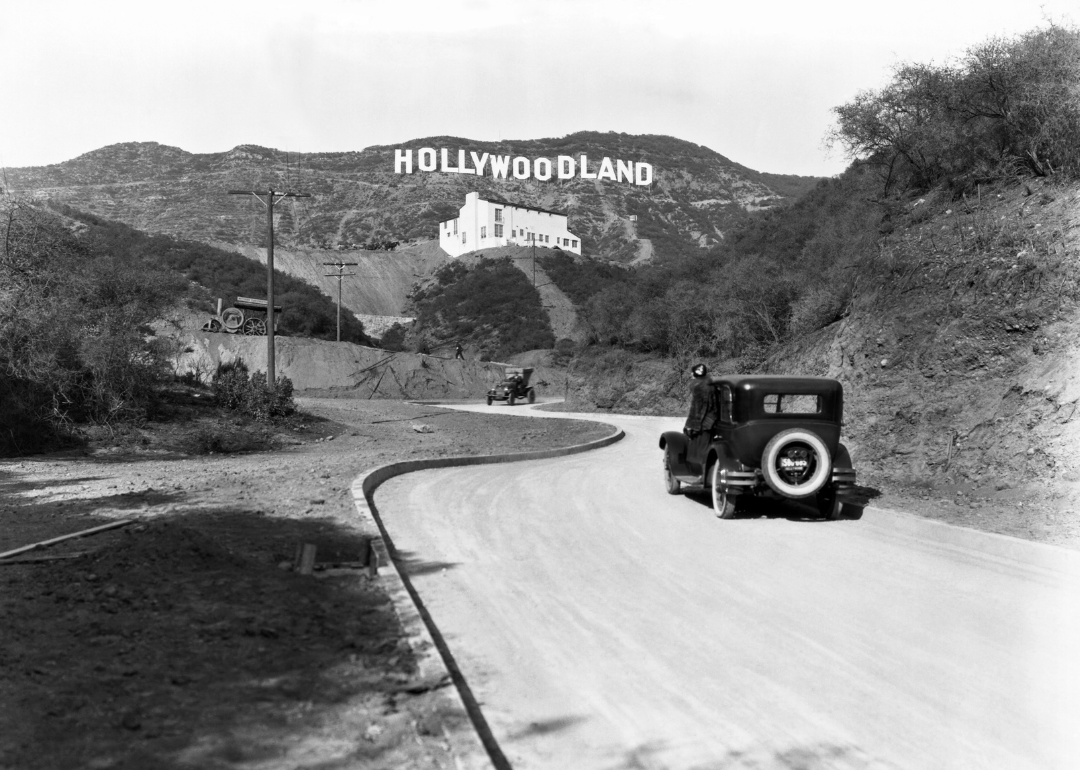 A car driving through the Hollywood Hills beneath the Hollywoodland sign.