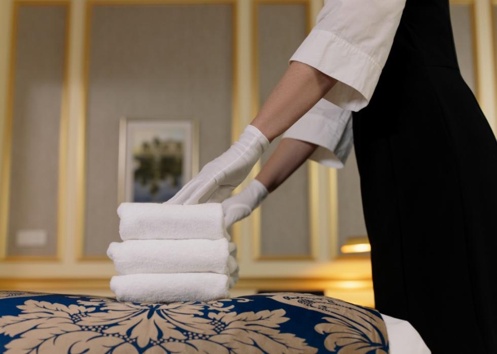 Closeup of maid putting folded towels on a hotel bed.