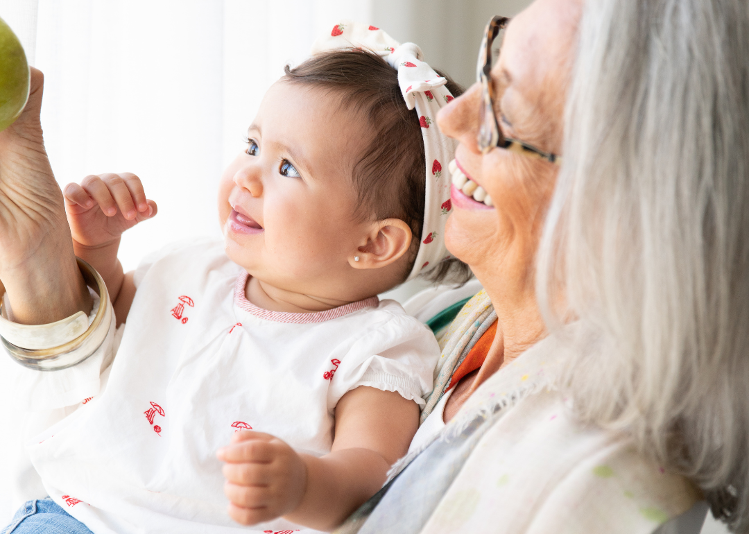 Grandmother holds granddaughter while smiling.