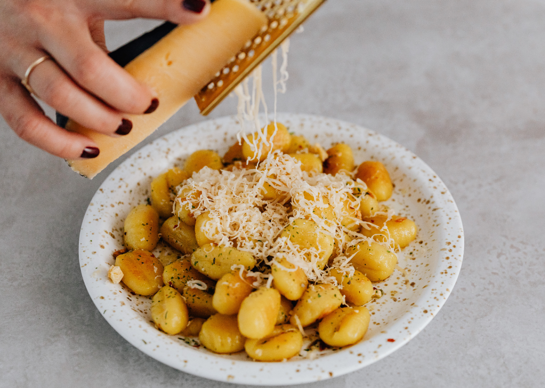 Closeup of a hand grating cheese over a plate of gnocchi.