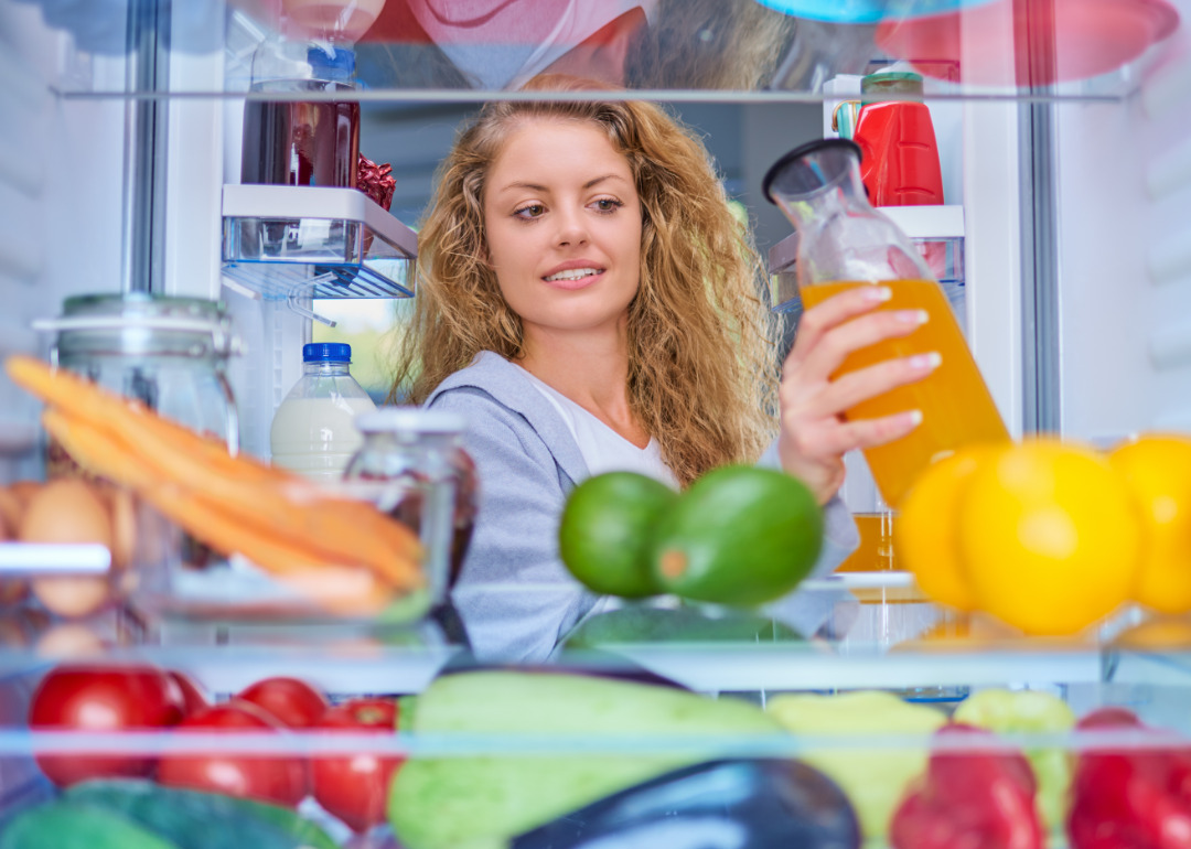 View from inside of a refrigerator as a woman grabs a bottle of juice.
