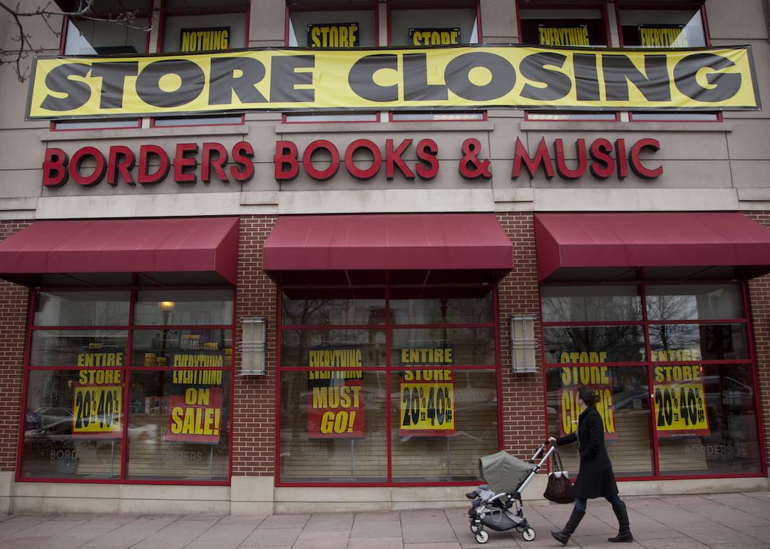 A person with a stroller walks by a "Store Closing" banner above a Borders Books & Music storefront. 