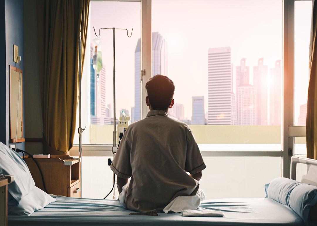 Cancer patient sits on hospital bed, looking out the window.