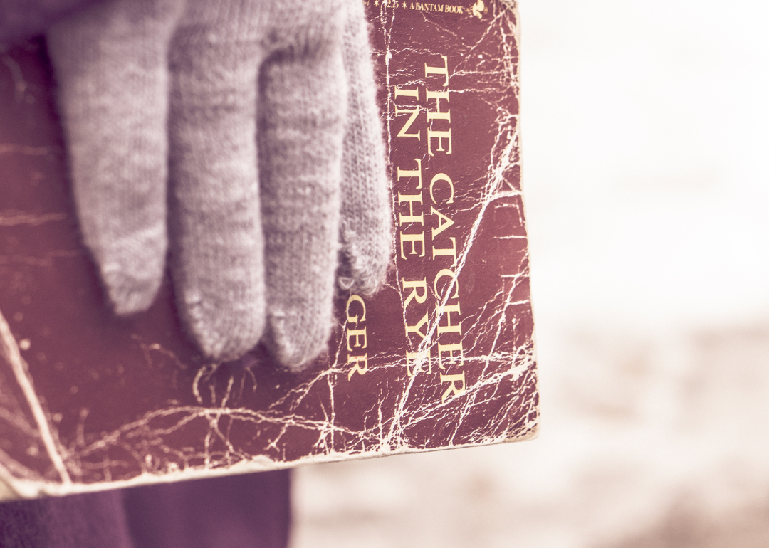 Closeup of a gloved hand holding an aged copy of "The Catcher in the Rye," the only novel J.D. Salinger wrote.