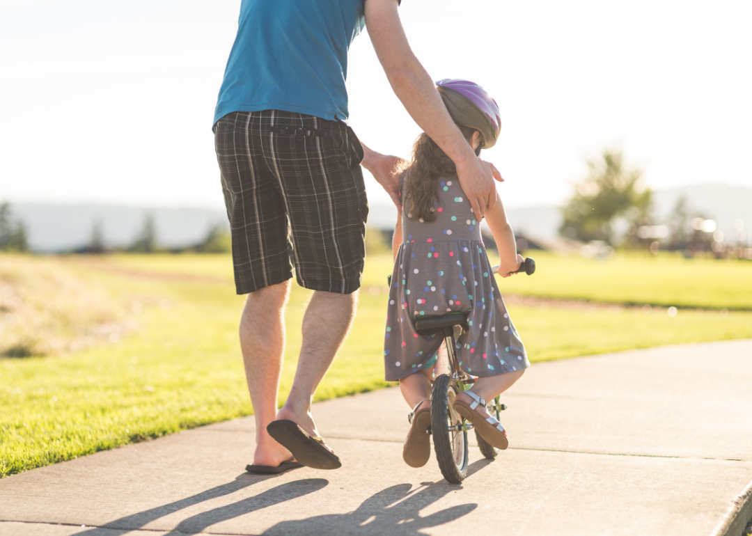 Young girl learning to ride bike with dad in the park.