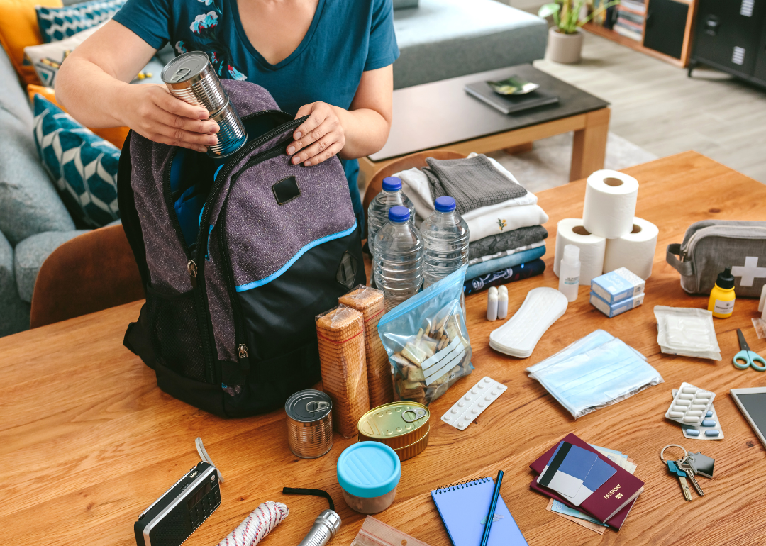 Woman putting cans of food in backpack to prepare for emergency.