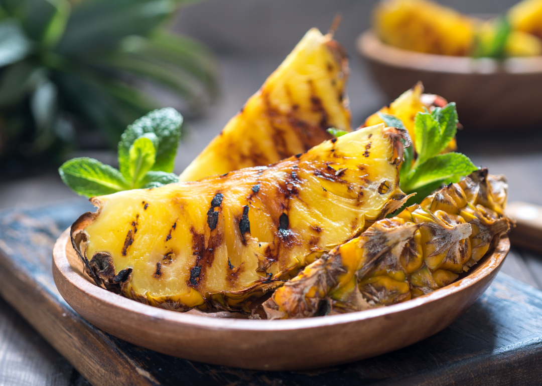 Grilled pineapple slices in a wooden bowl.