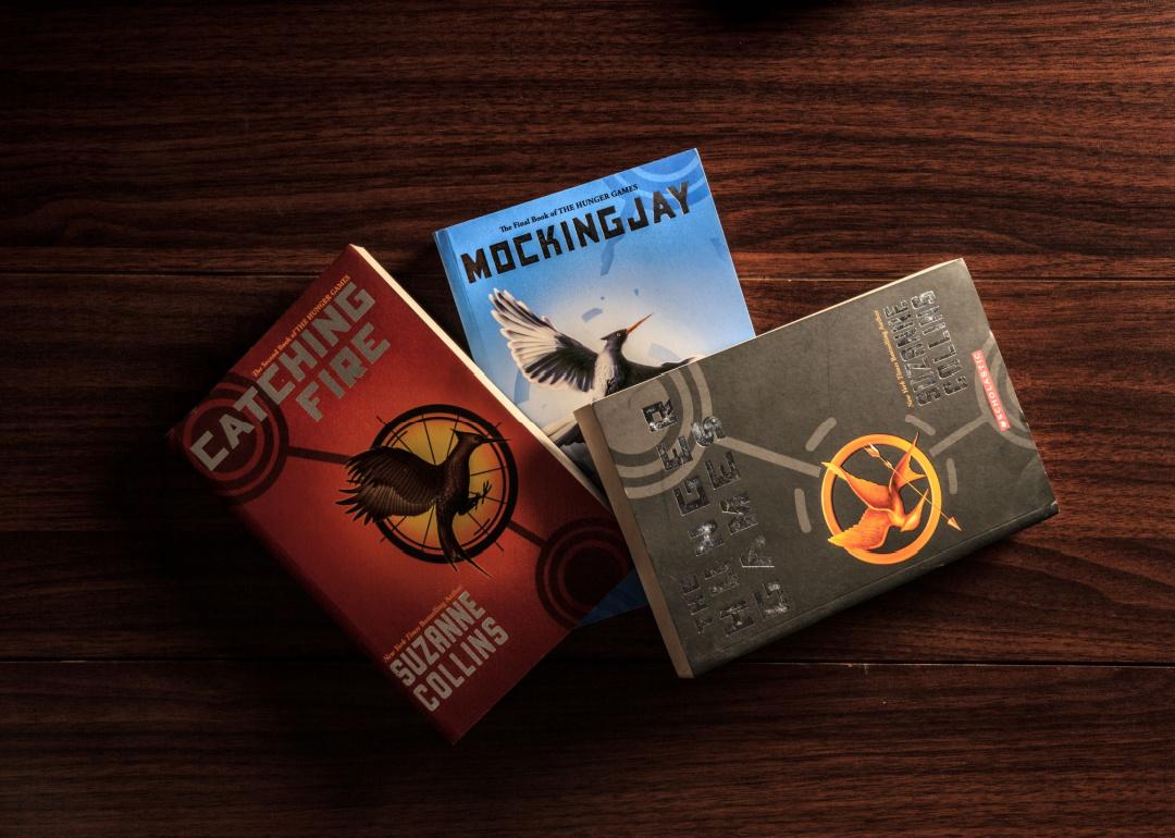 The three books of the sci-fi trilogy "Hunger Games," in order, "The Hunger Games," "Catching Fire,"and "Mockingjay," on a wooden table.