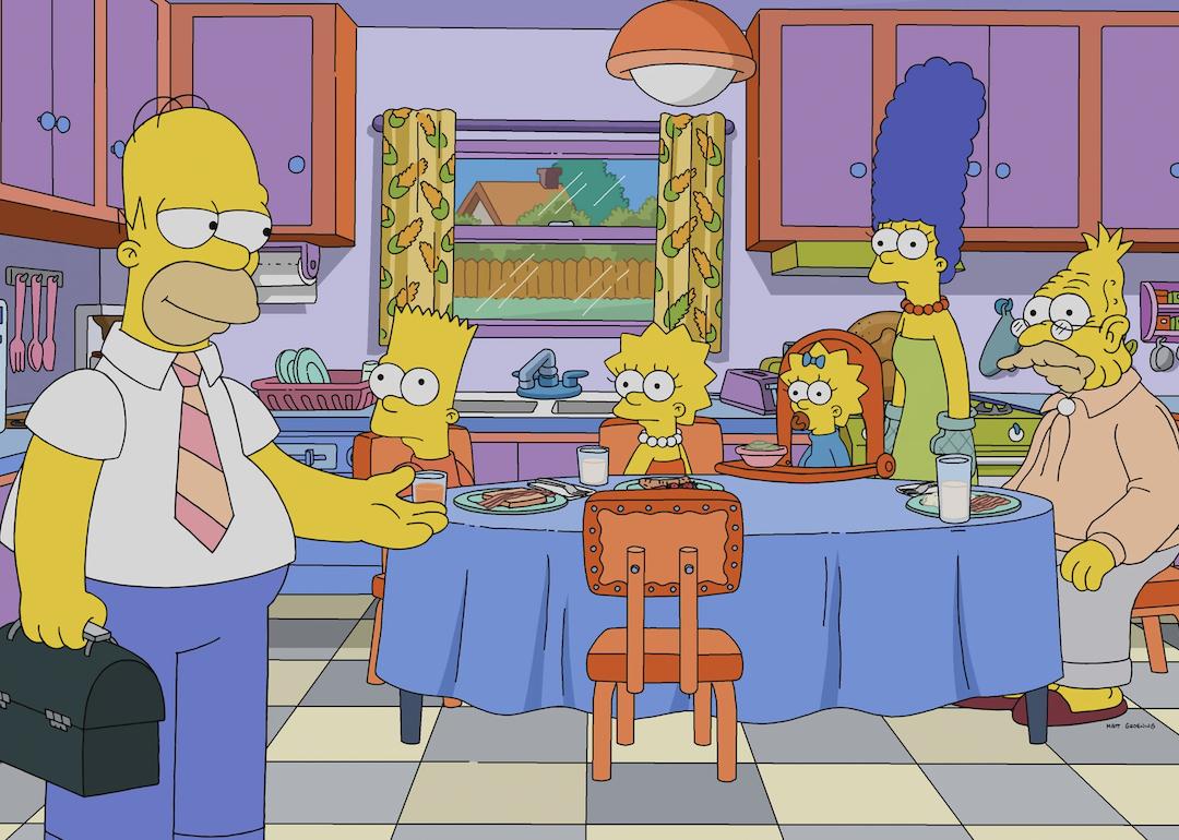 Homer Simpson stands in the kitchen while Bart, Lisa, Maggie, and Grandpa sit at the kitchen table, with Marge standing behind it.