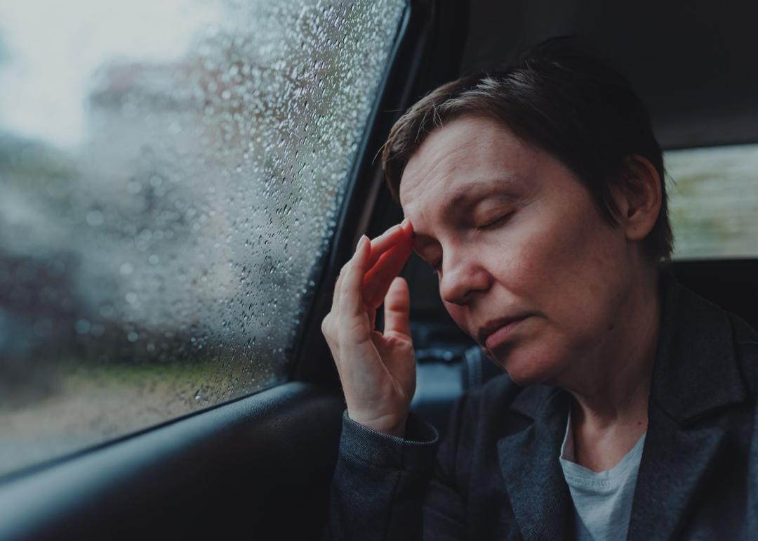 Businesswoman with severe headache sitting at the backseat of a car during a rain storm.