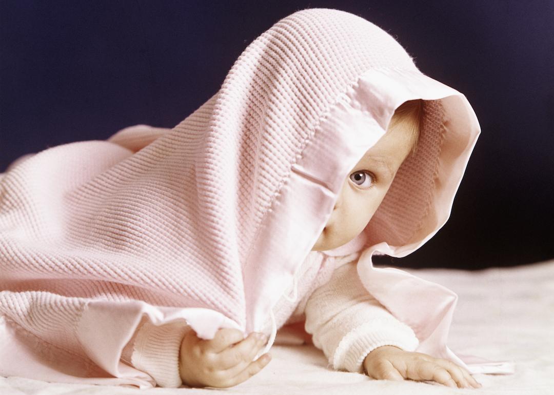 1980s baby peeking out from under a pink blanket, looking at the camera
