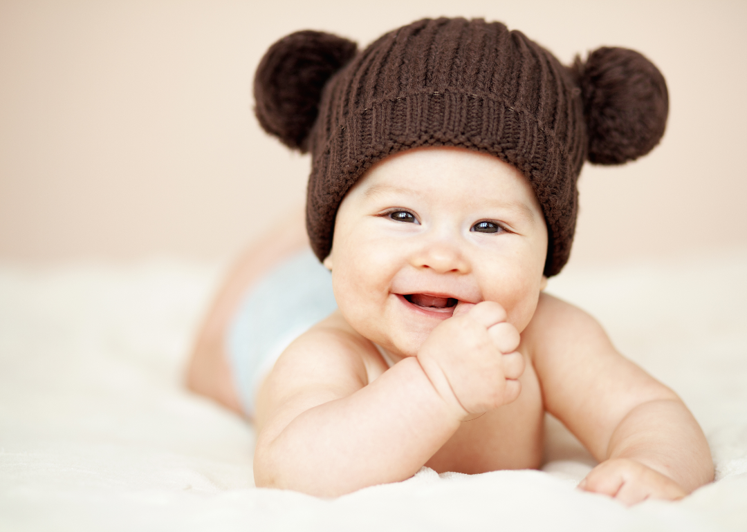 Baby laying on stomach in a diaper and brown knit hat