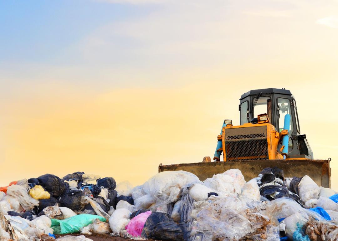Bulldozer in landfill with plastic bags and food waste