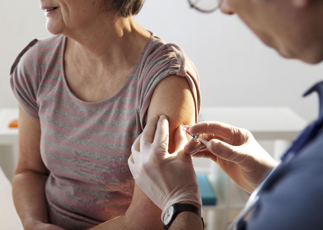 A closeup of a senior woman being vaccinated against the flu by a doctor in her left arm.