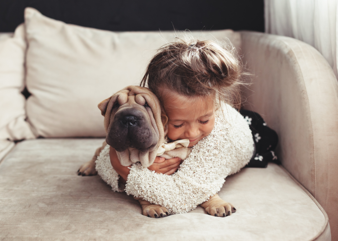 A young girl laying on a couch hugging her dog.