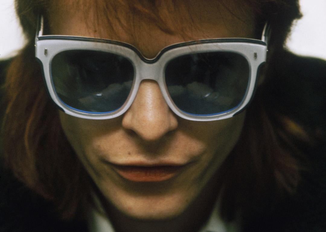 David Bowie's face close up with red spiky hair and white sunglasses circa 1974.