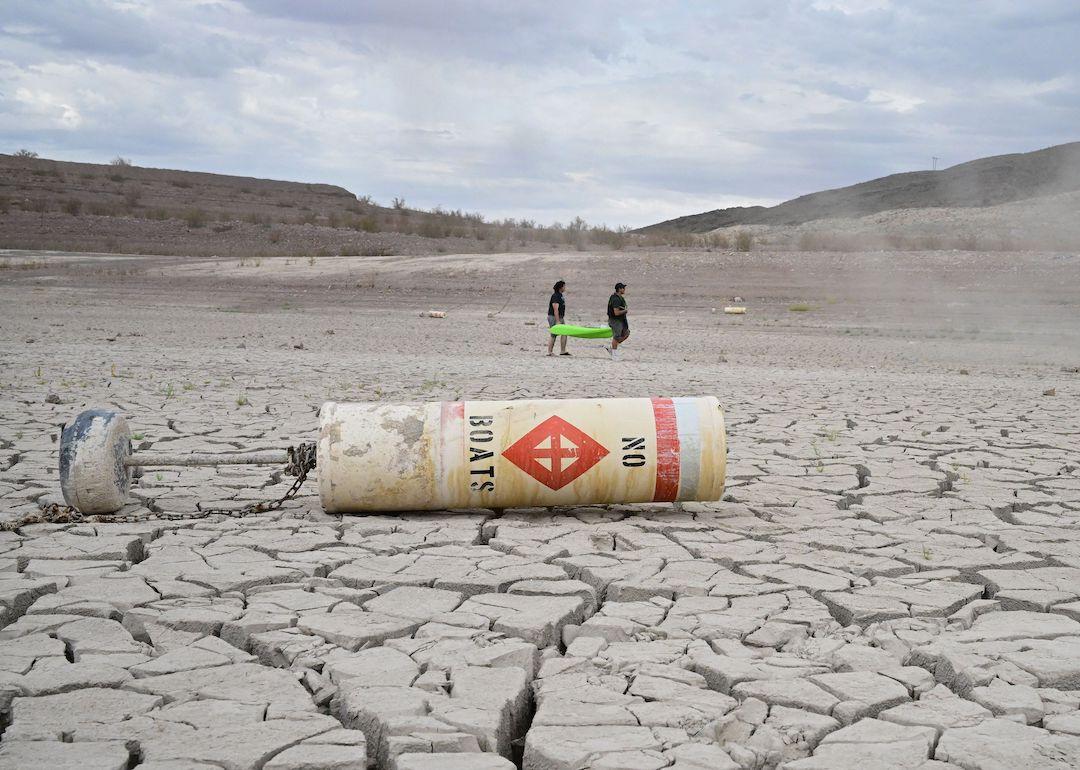 A buoy that reads 'no boats' lays on cracked dry earth in Nevada where water once was as people carry a boat further out to reach water at Lake Mead on July 23, 2022.