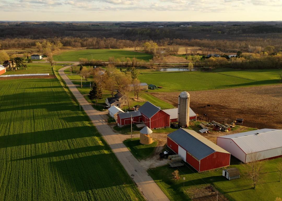 Aerial view of farmland with red barns in spring, a rural road, and agricultural fields in America.