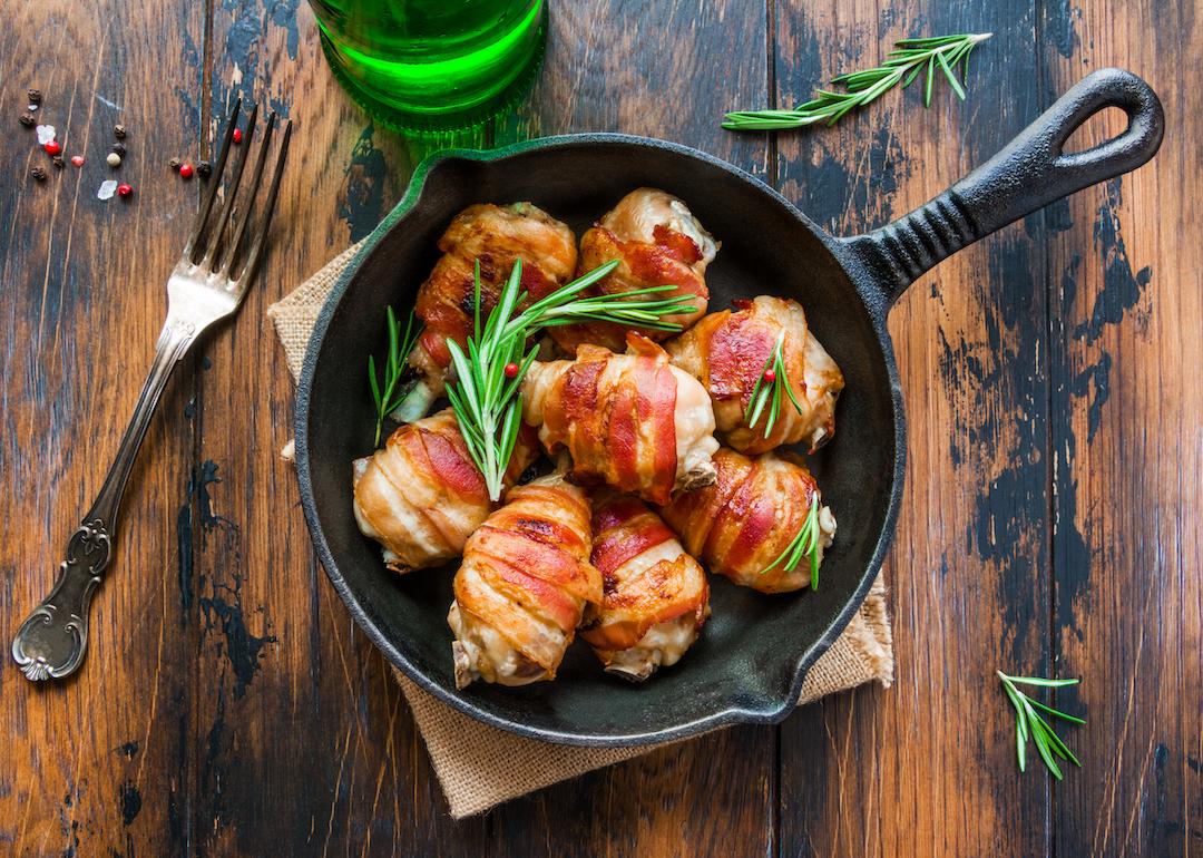 Bacon-wrapped chicken in a cast iron skillet on a wooden table.