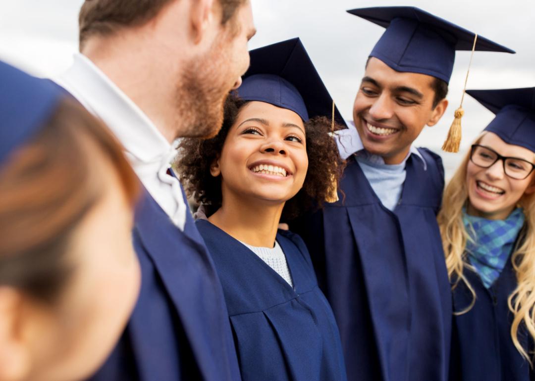College graduates embrace in navy blue caps and gowns at graduation ceremony.