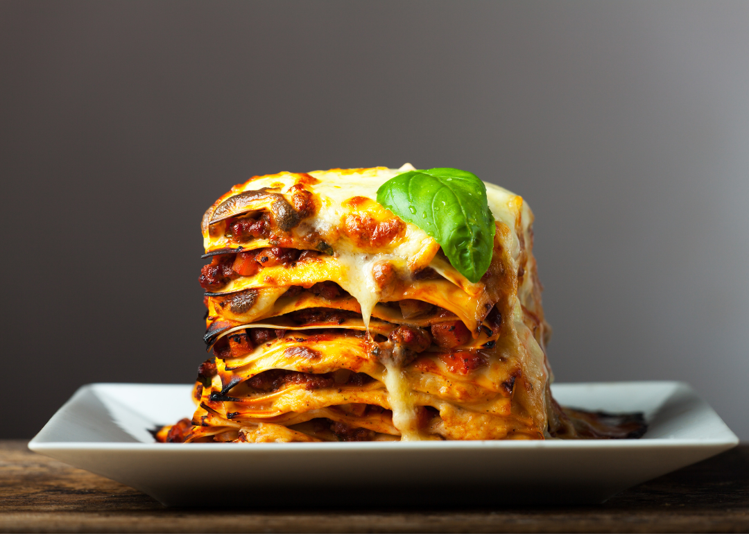 Eggplant lasagna piled high on a white plate in front of a dark gray background.