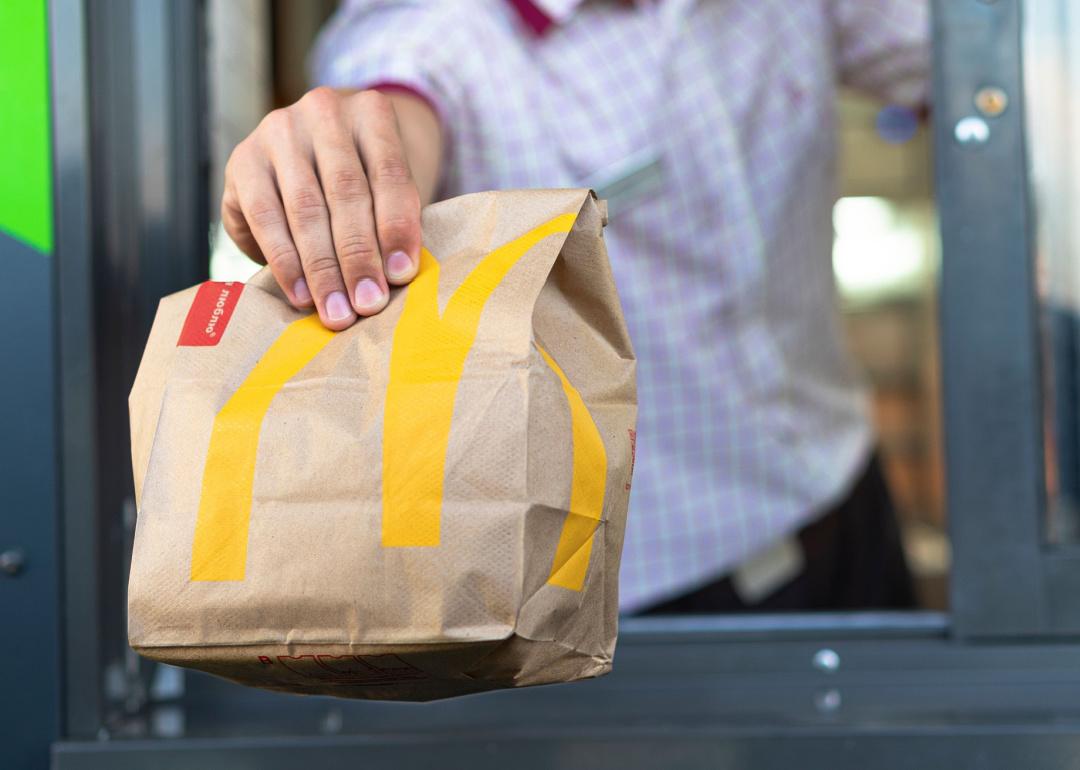 McDonald's worker holding a bag of fast food at the drive-thru window.