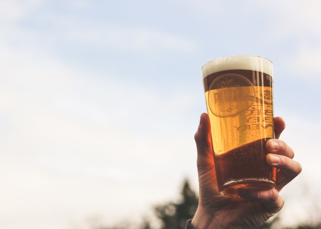 Closeup of a hand holding a glass of beer, raising it as if to toast.