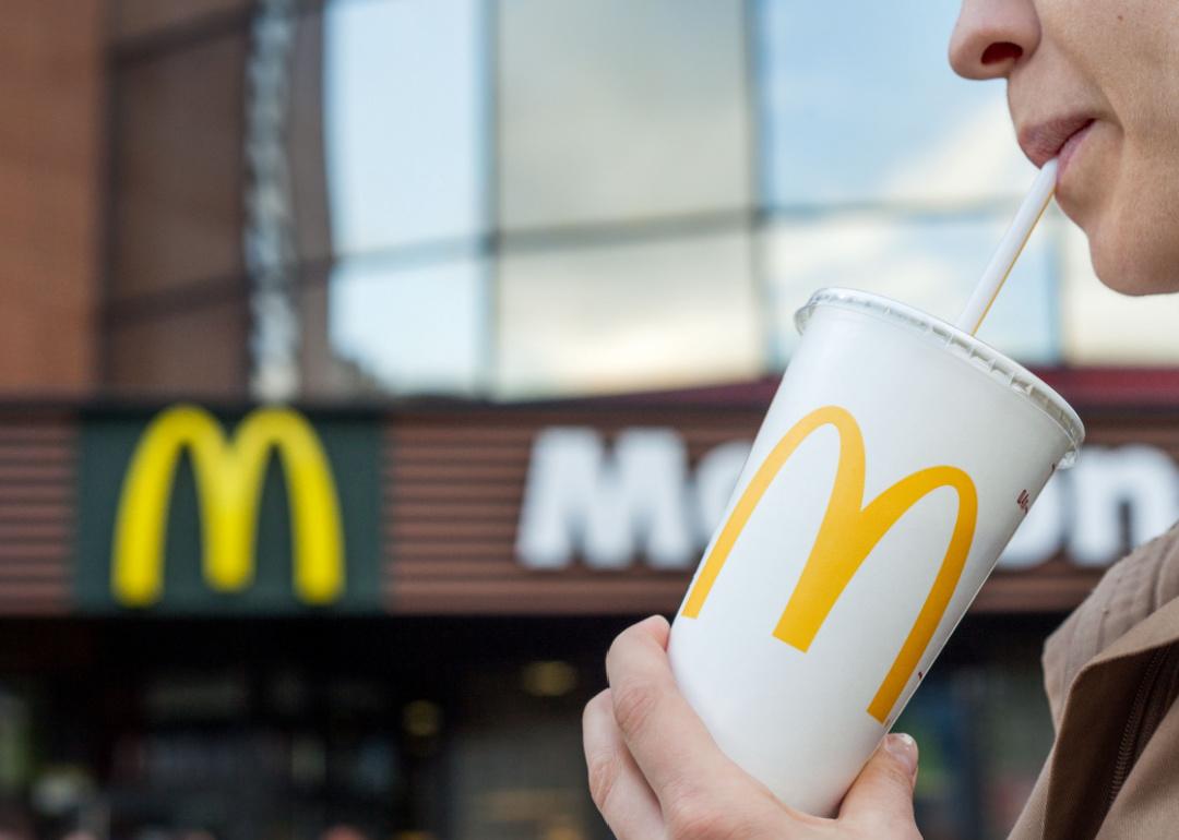 Person sips a McDonald's soft drink from a straw with golden arches in the background.