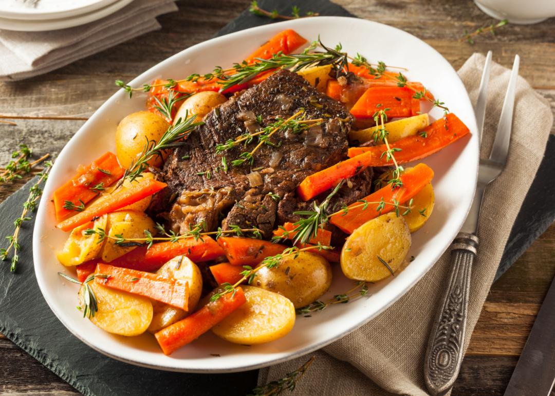 Homemade slow cooker pot roast with carrots and potatoes on a white plate.