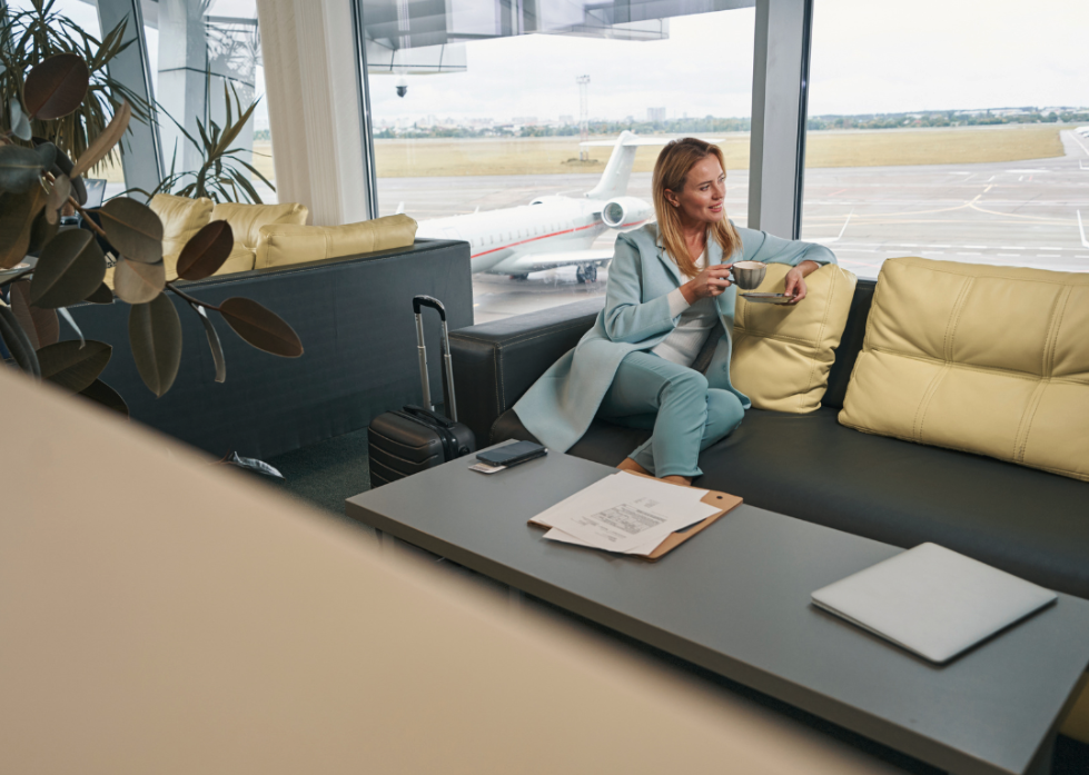 A person on a couch drinking coffee in an airport lounge or coworking space.