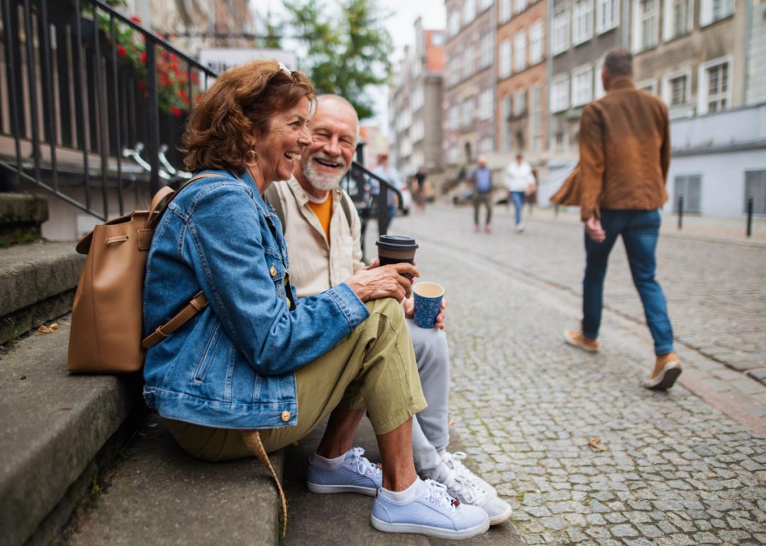 Senior couple sitting on stairs and having a coffee outdoors in a city.