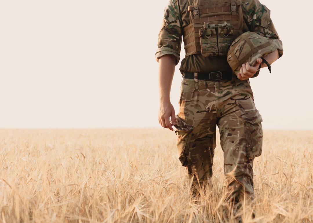 US army soldier holding their helmet and standing in a field.