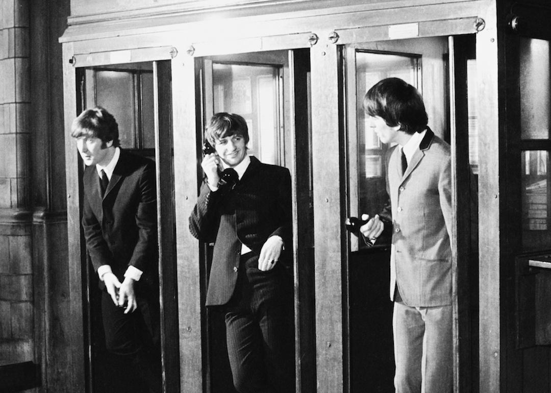 From left to right, Beatles band members John Lennon, Ringo Starr, and George Harrison stand in the telephone booths at Marylebone Station in London during the filming of their mockumentary 'A Hard Day's Night' in 1964.