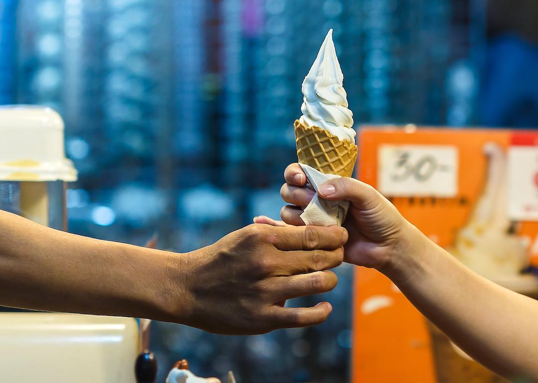 Server hands vanilla soft-serve ice cream cone to customer.