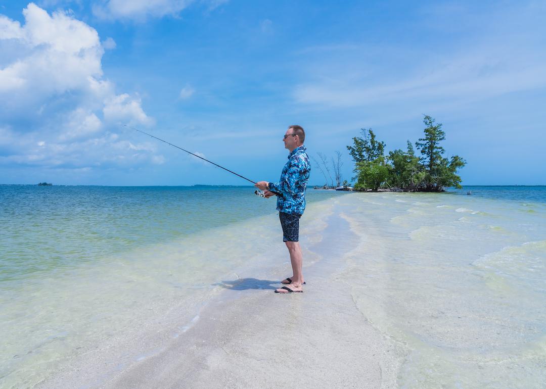 Retired person in rash guard standing on white sand fishing in Indian River Island, Florida.