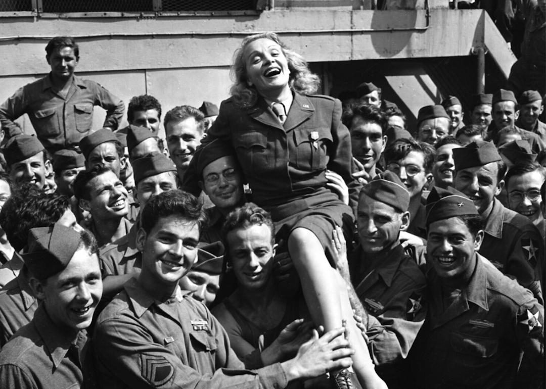 Actor and musician Marlene Dietrich is held up by soldiers from the USS Monticello in New York in 1945.