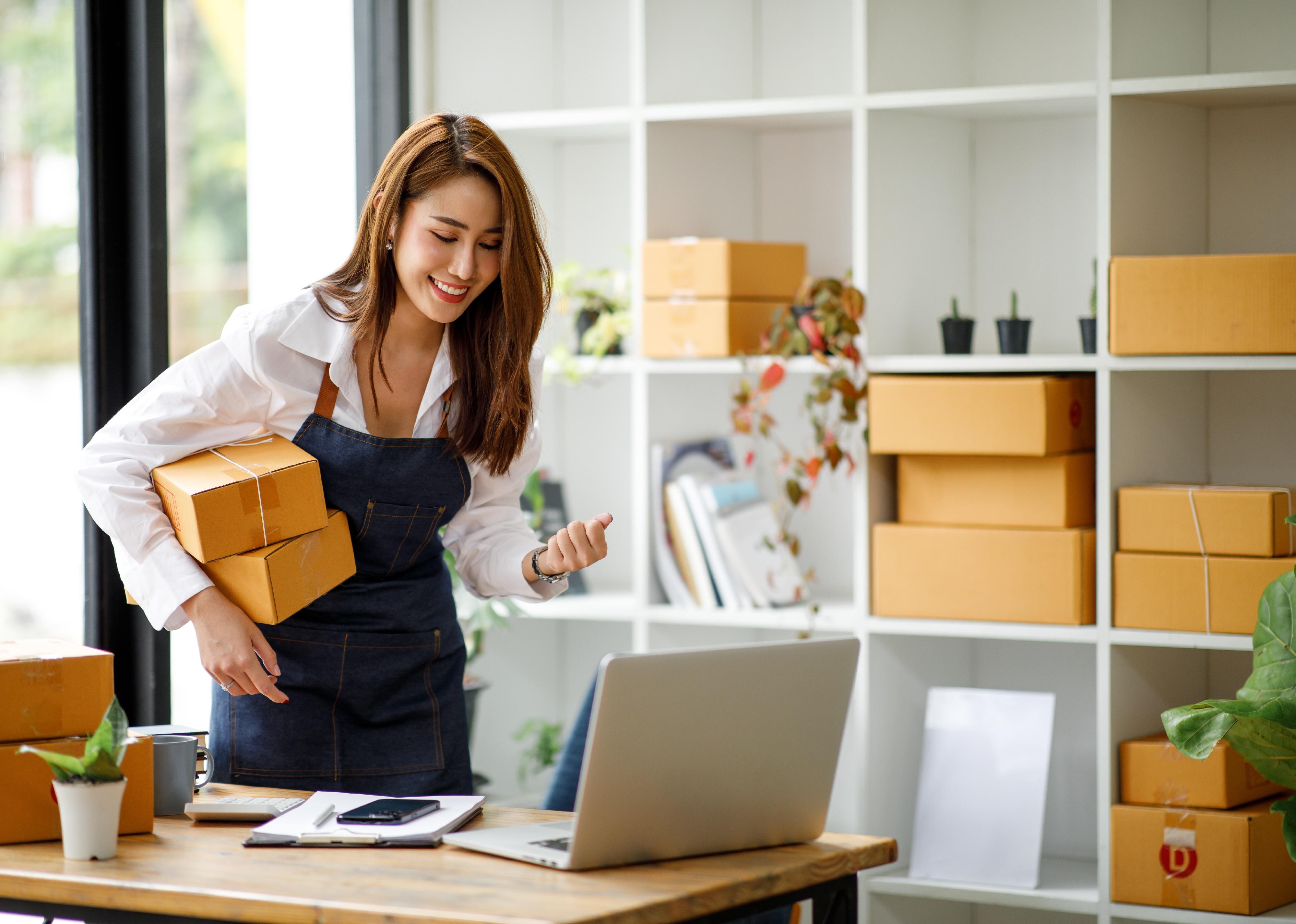 Woman wearing an apron stands in front of work space holding boxes.