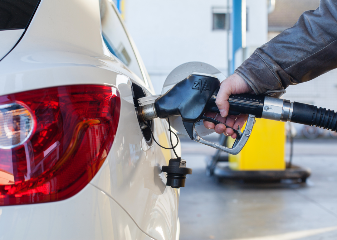 Driver filling up gas tank of white car at gas station.