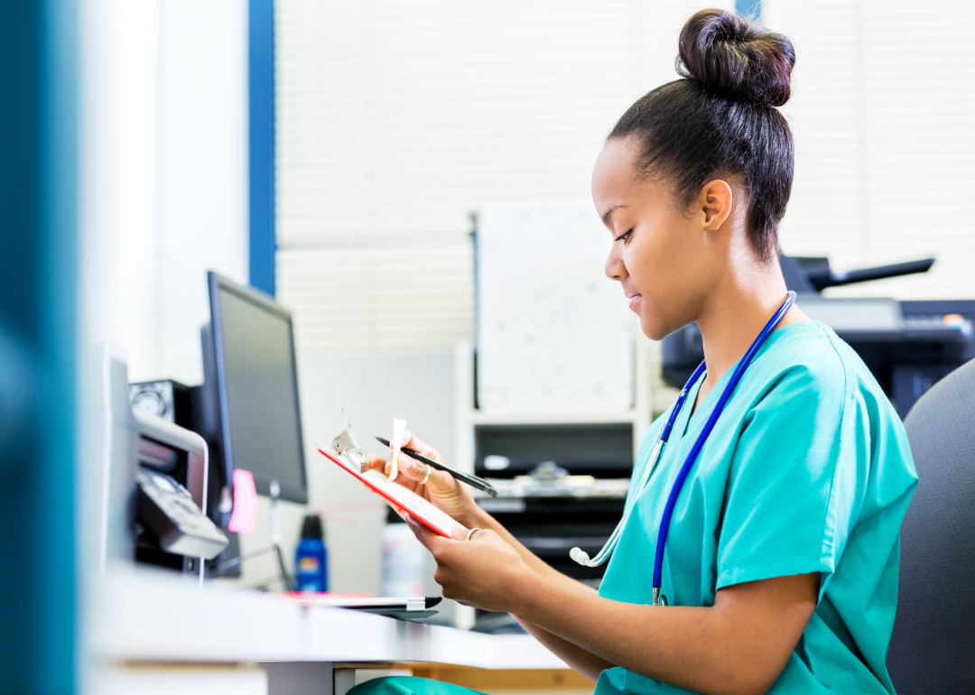 A nurse seated at a desk checking results on a tablet.