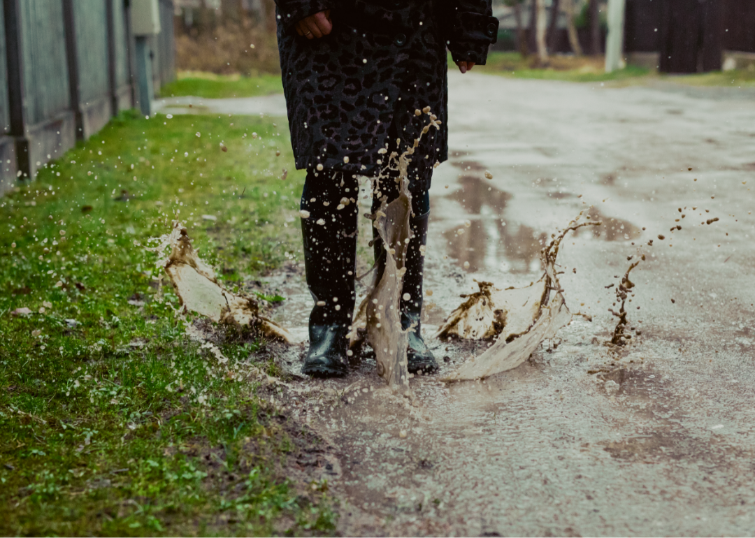 Person sloshes in a puddle in their black rain boots.
