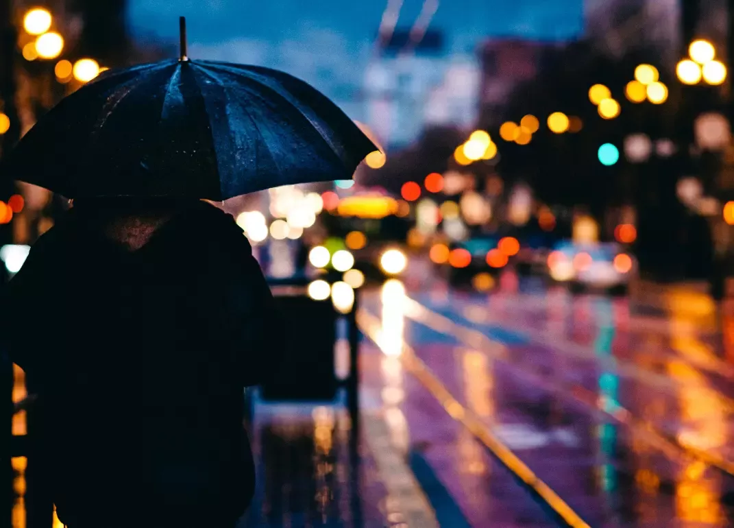 Person standing with an umbrella in the rain at night.