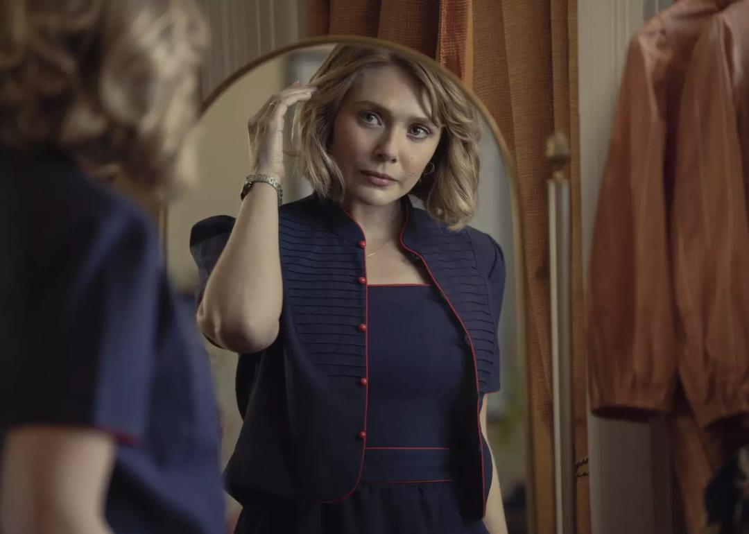 Actor Elizabeth Olsen looks in the mirror and tucks her hair behind her ear as Candy Montgomery in the HBO miniseries 'Love & Death.'