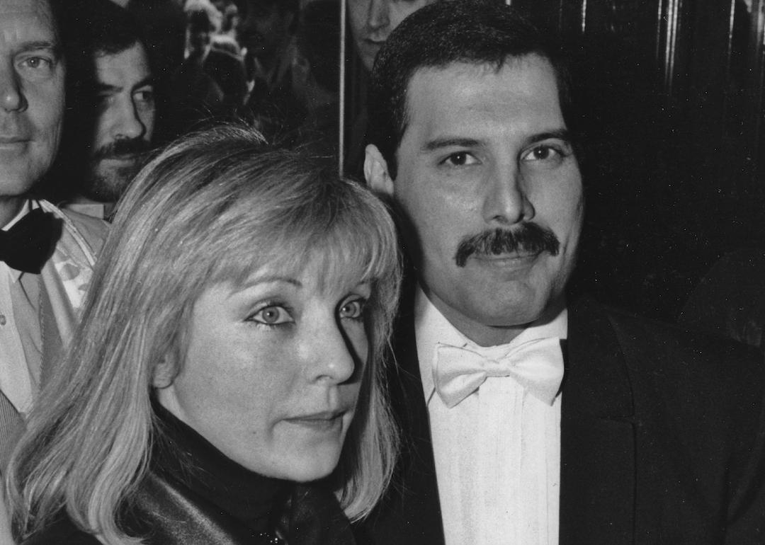 Singer Freddie Mercury of Queen with Mary Austin at an afterparty in London for 'Dave Clark's Time - The Musical' in 1986. Behind them is Queen's manager Jim Beach.