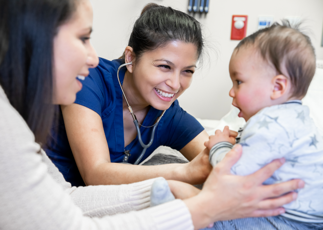 A nurse practitioner examines a baby while their parent holds them.