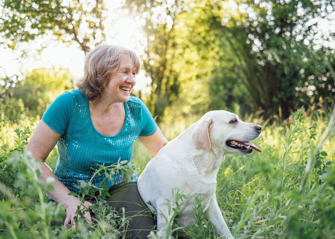 Elderly person wearing a turquoise t-shirt sits next to her Labrador dog in the grass